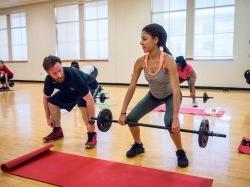 A female lifting a barbell and a man next to her instructing her.