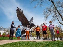 Six students in masks standing outside in front of Montclair State's hawk statue
