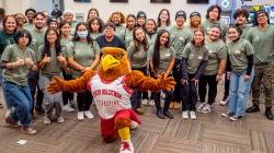 A Red Hawk mascot poses for a photo with students.