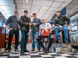 Five men from rock bands pose in a retro diner.
