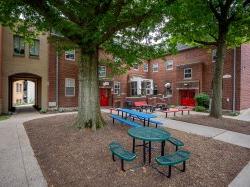 树木为庭院和绿地提供阴凉, 蓝色和红色的野餐桌，以及砖砌建筑外的户外座位.