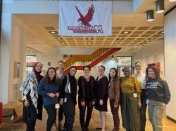九名学生和一名教授站在十大博彩推荐排名州立大学的横幅下，横幅上展示着红鹰.